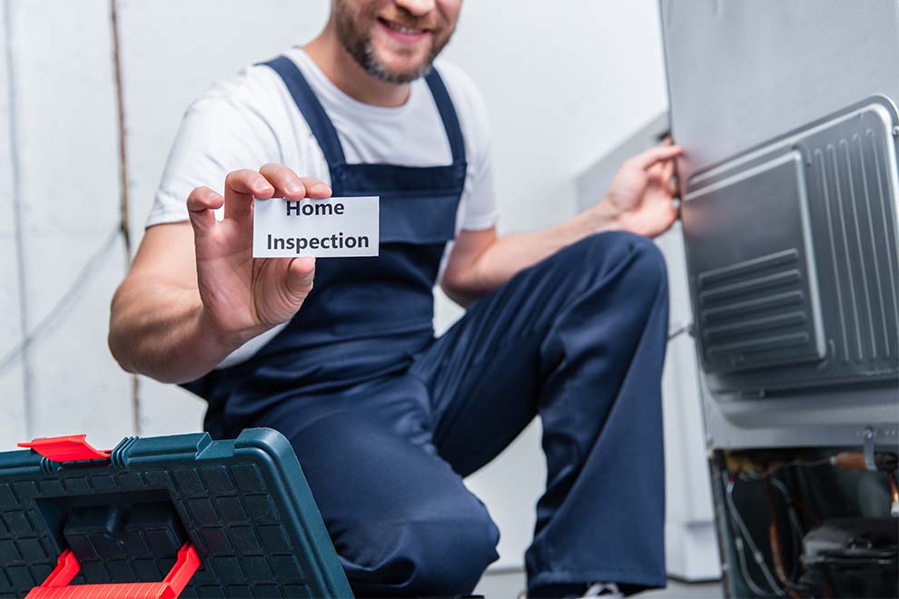 um homem segurando um pequeno papel escrito home inspection, enquanto está na frente de um eletrodoméstico para verificar se precisa de conserto